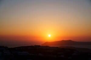 Sunset over hilly coastal landscape with silhouettes and sea, orange and yellow sky.