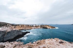 Coastal cliffs, deep blue sea, rocky shore, white buildings, cloudy sky.