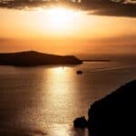 Sunset over calm sea with island silhouettes, warm sky, and boat wake in the water. 10 Amazing Days in Greece