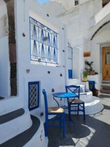 Outdoor blue table and chairs, white building, blue grille, steps, door, plants, Mediterranean style.