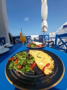 blue table, omelet with peppers, salad, orange juice; clear sky background.