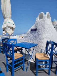 Blue chairs and table on a terrace with white architecture and blue sky, Mediterranean setting.