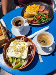 scrambled eggs, bacon, bread, salad, Greek salad, two coffee cups.