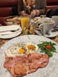 Breakfast with fried eggs, ham, arugula, juice, coffee, fruit salad, bread, and dried flowers.