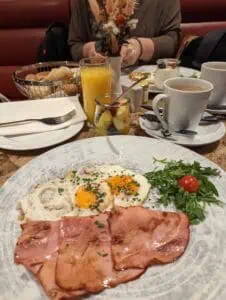 Breakfast with fried eggs, ham, salad, coffee, orange juice, fruit salad, bread rolls, flowers.