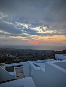 Sunset over coastal landscape with whitewashed Mediterranean structures in the foreground.