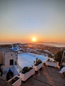 Sunset over a coastal town with white buildings and rooftop planters in the foreground.