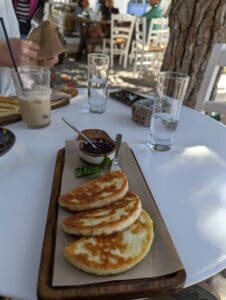 Grilled cheese on board with sauce, drink, and water glasses in an outdoor dining setting.