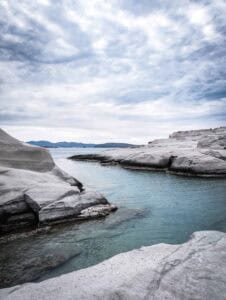 Overcast sky over tranquil coast with smooth rock formations and shallow clear water.