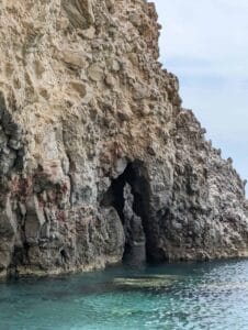 Rocky coastal cliff with a natural archway over turquoise water and overcast sky.