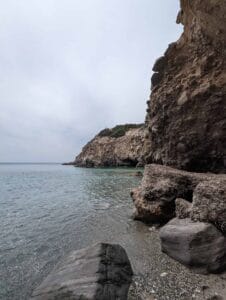 Rocky coast with jagged cliffs and calm sea under an overcast sky, gentle waves at shore.