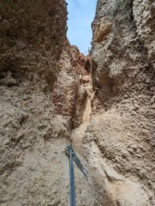 Narrow, rocky path with cliffs and frayed rope under a clear blue sky.