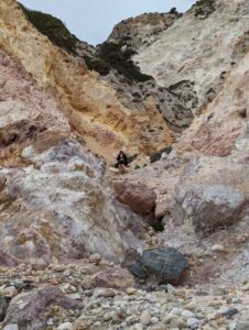 Person among colorful, textured rock formations with vegetation and scattered small stones.