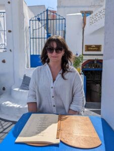 Person in sunglasses seated at blue table with open menu at outdoor cafe "Penelopes."