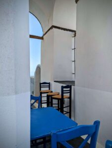 Outdoor seating area with blue chairs and tables, white walls, and a clear sky view.