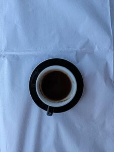 Black coffee cup on textured white cloth with black saucer.