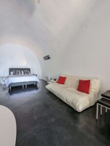Minimalist room with white curved ceiling, bed, sofa with red cushions, and dark flooring.