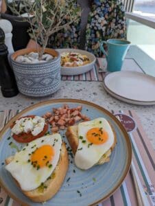 Breakfast with sunny-side-up eggs on toast, diced ham, tomato, cheese on blue plate, plant nearby.