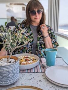 Person in sunglasses, floral shirt at table with meal, turquoise mug, and potted plant.