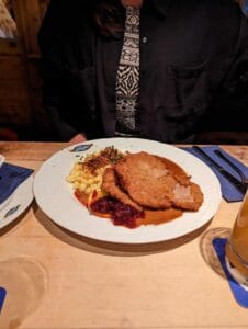 Person at table with breaded meat cutlet, pasta, red sauce, and drink on the side.