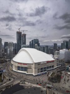 Rogers Centre Amidst City Construction Large stadium with a dome, high-rise buildings, cranes, and overcast sky. "Rogers Centre" visible.