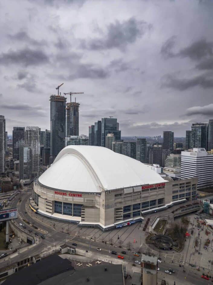 Large stadium with a dome, high-rise buildings, cranes, and overcast sky. "Rogers Centre" visible.