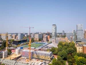 Aerial view of cityscape with skyscrapers, cranes, stadium, trees, and clear sky.