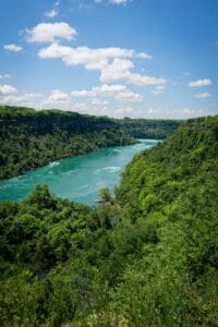 River flowing between green forests under a blue sky with clouds.