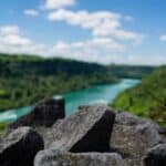 Sharp rocks in focus, river and green hills blurred in background under blue sky with clouds.