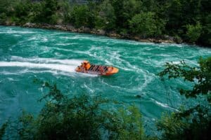 Orange jet boat on turquoise waters, surrounded by lush green forest and rocky shoreline.