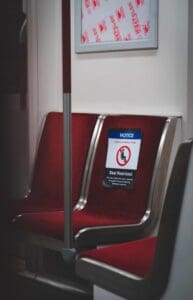 Red transit seats, one with COVID-19 restriction sign, pole and signage frame visible.