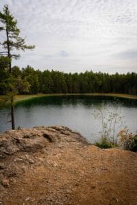 Small round lake, dense forest, rocky terrain, cloudy sky, shrubs, trees, serene landscape