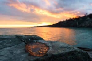 Coastal sunset with rocky foreground, puddle, calm sea, and vibrant sky colors.