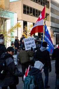 Protest on city street with signs, Canadian flag, and tall buildings in background.