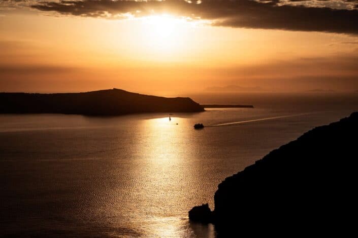 A golden sunset over the Caldera in Santorini. A boat can be seen making it's way back to the port