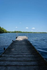 Wooden dock extending over a rippling lake toward a tree-lined shore under a blue sky.